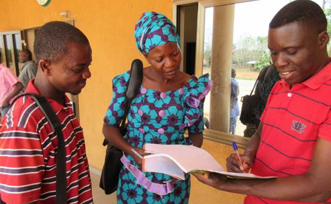 Three people reading a book in Ghana