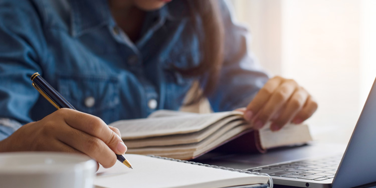 Closeup of someone reading a book and writing in a notebook